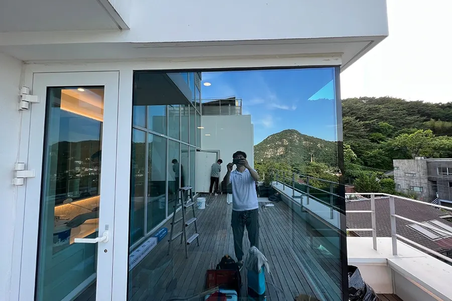옥상 테라스 모서리 통유리, 필름 시공이 완료되어 거울처럼 주변 산세가 비치는 모습