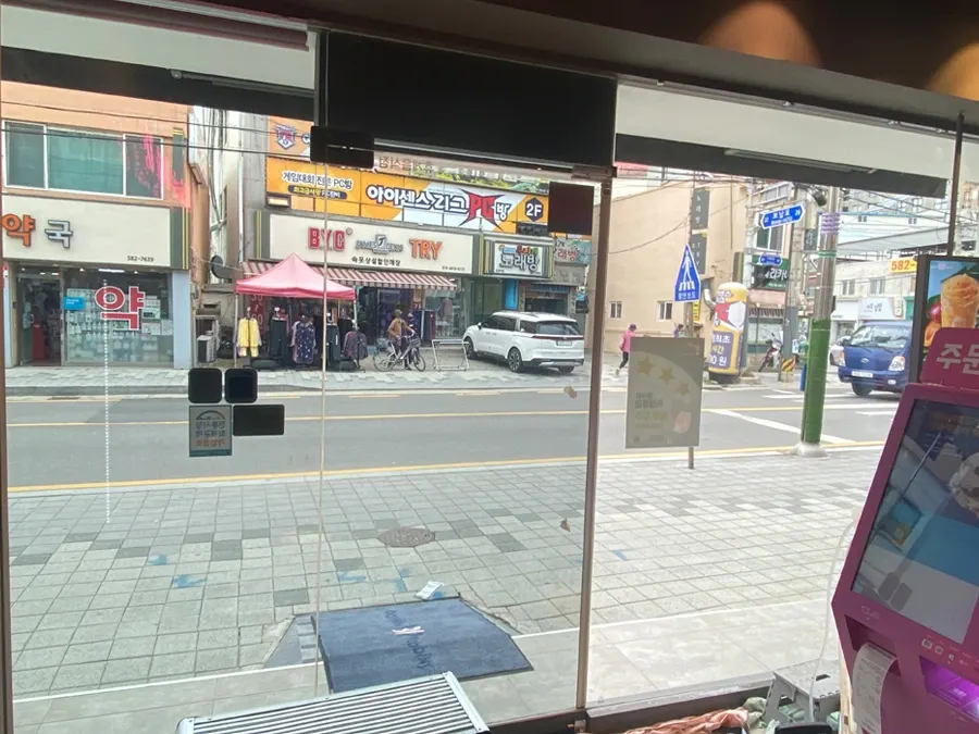 필름 시공 전 매장 내부에서 바라본 통유리창, 반사 없이 거리가 그대로 비치는 모습