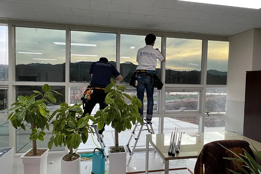 시공 기사들이 사다리에 올라 통유리창에 필름을 부착하는 모습