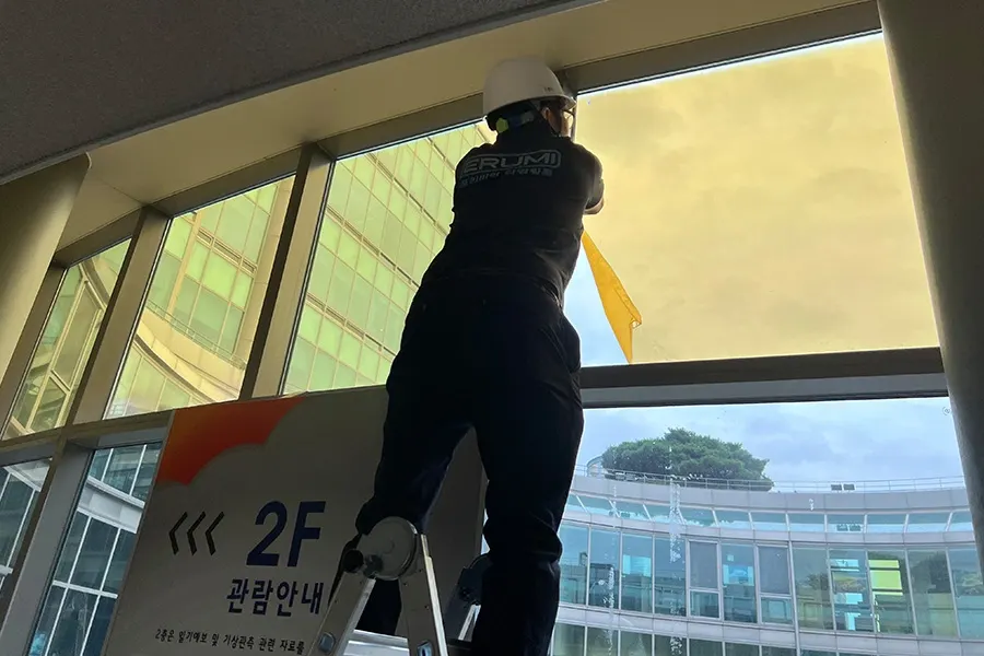 작업자가 필름 원단을 유리에 대고 실제 시공될 색상과 톤을 확인하는 모습