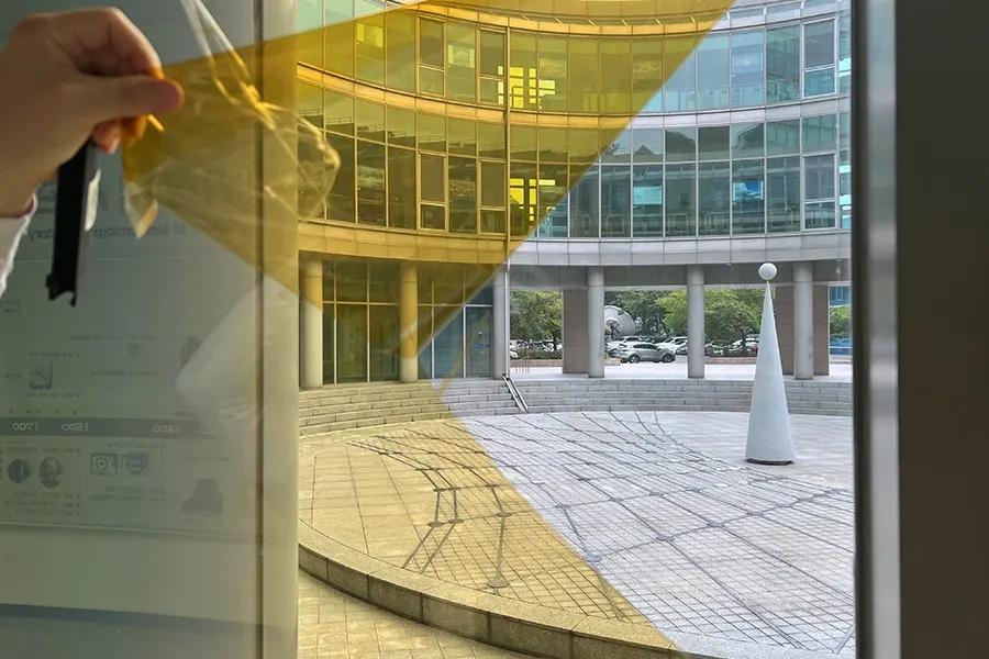 2층 창호 상단에서 필름을 부착하는 작업자, 시공이 진행된 유리창에 옅은 색상이 감도는 모습