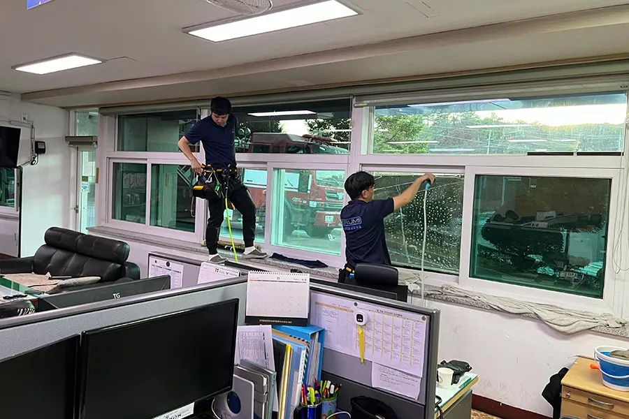 시공 중인 모습, 작업자가 창호 상단에서 필름을 부착하는 장면